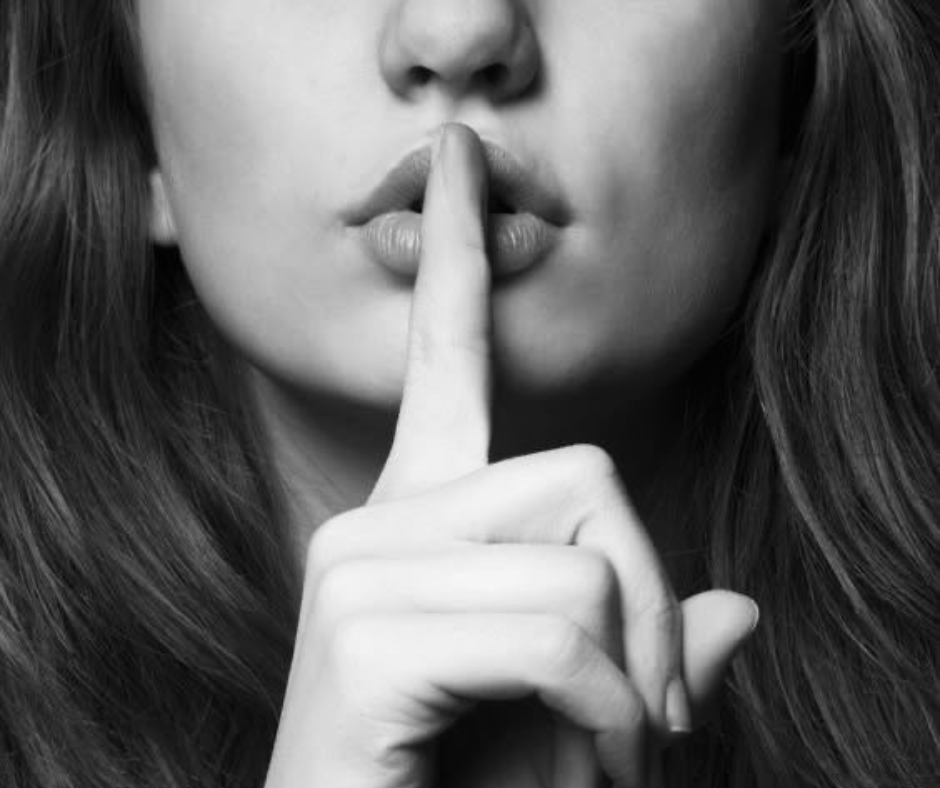 Black and white close-up of a woman with a finger to her lips, used to represent the bridal hair secret behind natural, long-lasting wedding hair.