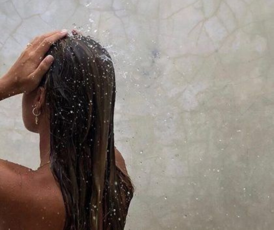 Woman rinsing wet hair in the shower, used to illustrate scalp health and bridal hair preparation before clip-in extensions.